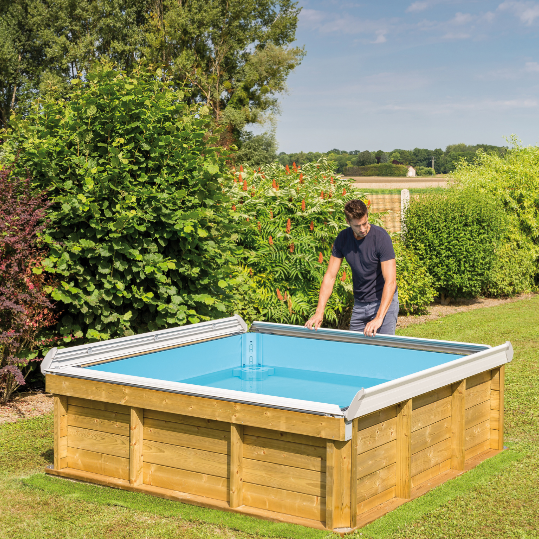Piscina de madera Pistoche rectangulara en jardín, con tapa corrediza y hombre ajustando borde superior.