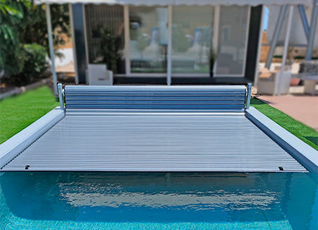 Terra Lite: tapa enrollable para piscina desplegada, cubriendo el borde y reflejo azul del agua.